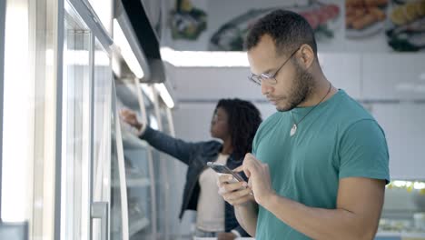 hombre afroamericano enfocado leyendo la lista de compras en su teléfono inteligente