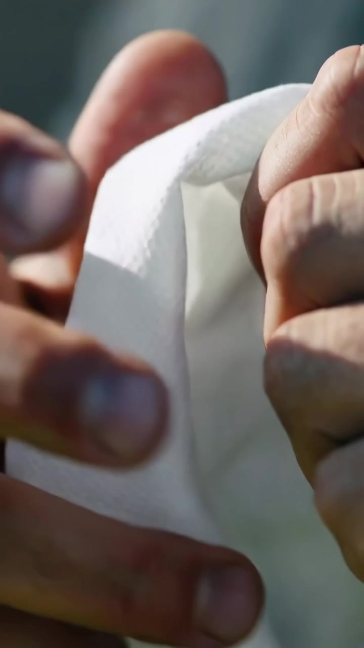 Vídeo vertical: Segurando as bordas do tecido, mãos puxando e dobrando-o em close-up ao ar livre, prendendo