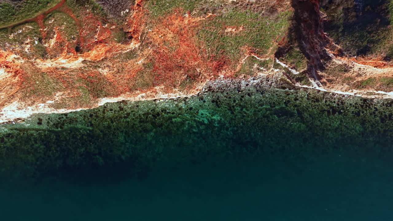 Coastline view showing red cliffs, clear water, and green vegetation in a natural landscape during daytime