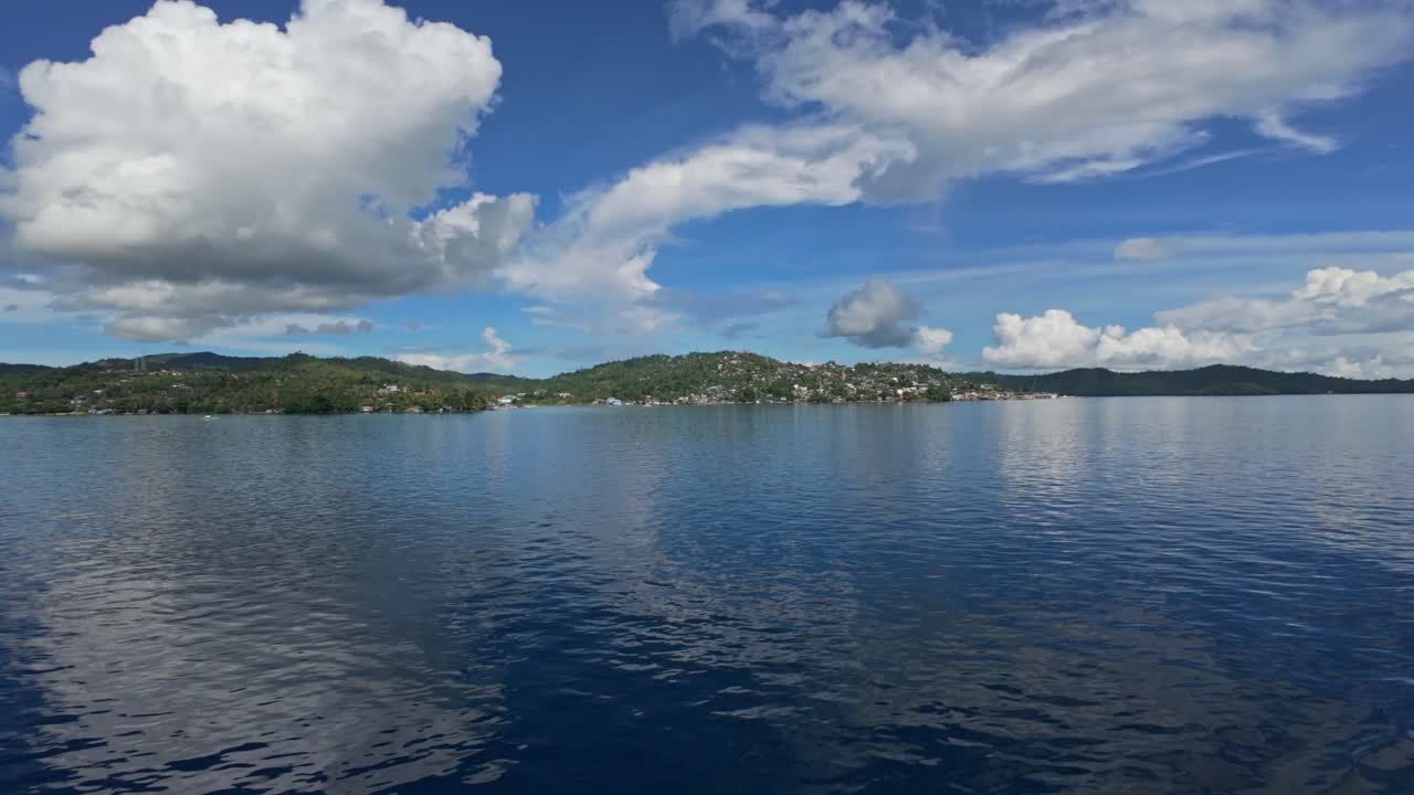 Wide view of San Jose town on Dinagat Island seen from ferry in motion across calm sea.