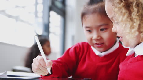 two infant school girls drawing with tablet computer and stylus in class, close up, rack focus