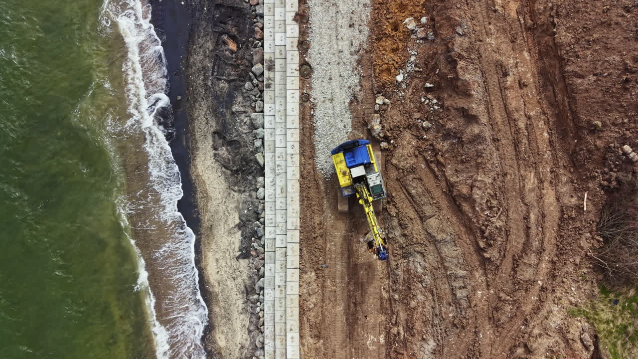 Costruzione di una diga foranea lungo la costa con macchinari al lavoro vicino alla riva durante le ore diurne.