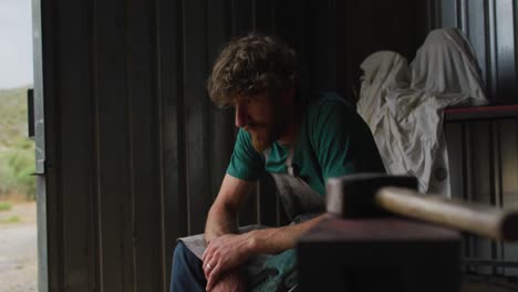 tired caucasian male blacksmith taking rest in workshop