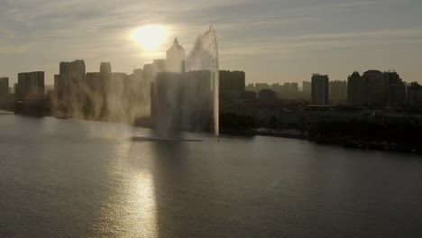 sunrise, golden hues, reflection across the songhua river, city waking up in shadows, clear sky and famous 160m high water fountain casting mist in the sun rays