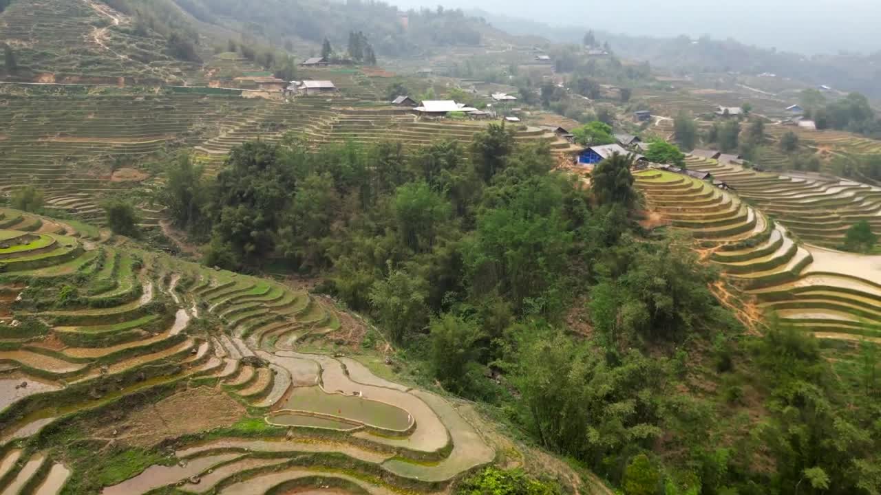 Aerial view of earthy rice terraces with intricate layers shaped into mountain slopes, bordered by trees and partially flooded plots prepared for seasonal planting.