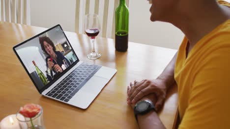 Mixed-race-man-sitting-at-table-using-laptop-making-video-call-with-male-friend