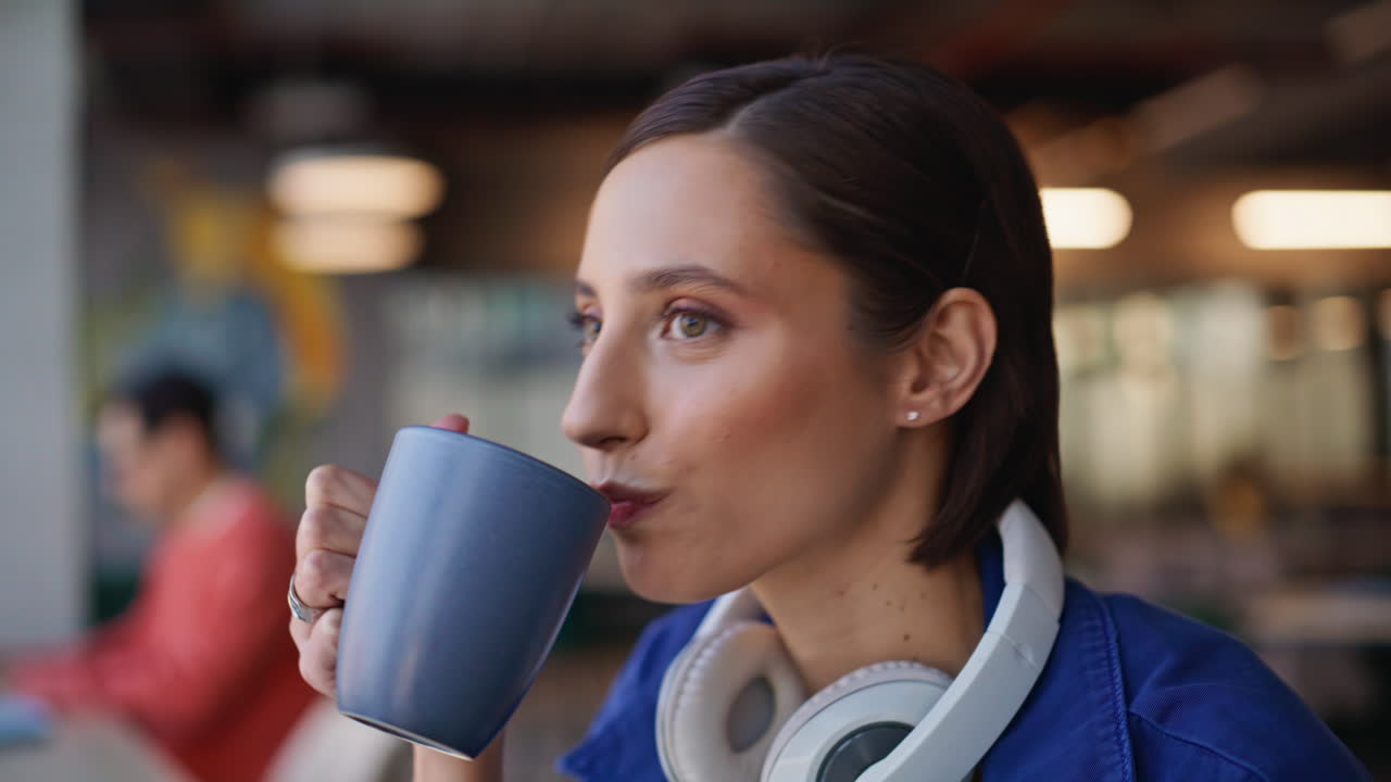 Dreamy girl sipping tea sitting cozy cafeteria with headphones on neck closeup