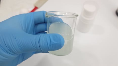 close-up view of a gloved hand holding a beaker of clear liquid in a laboratory setting