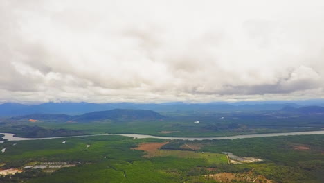 Drone-view-of-a-valley-with-a-river-and-mountains-in-the-background-on-a-cloudy-day