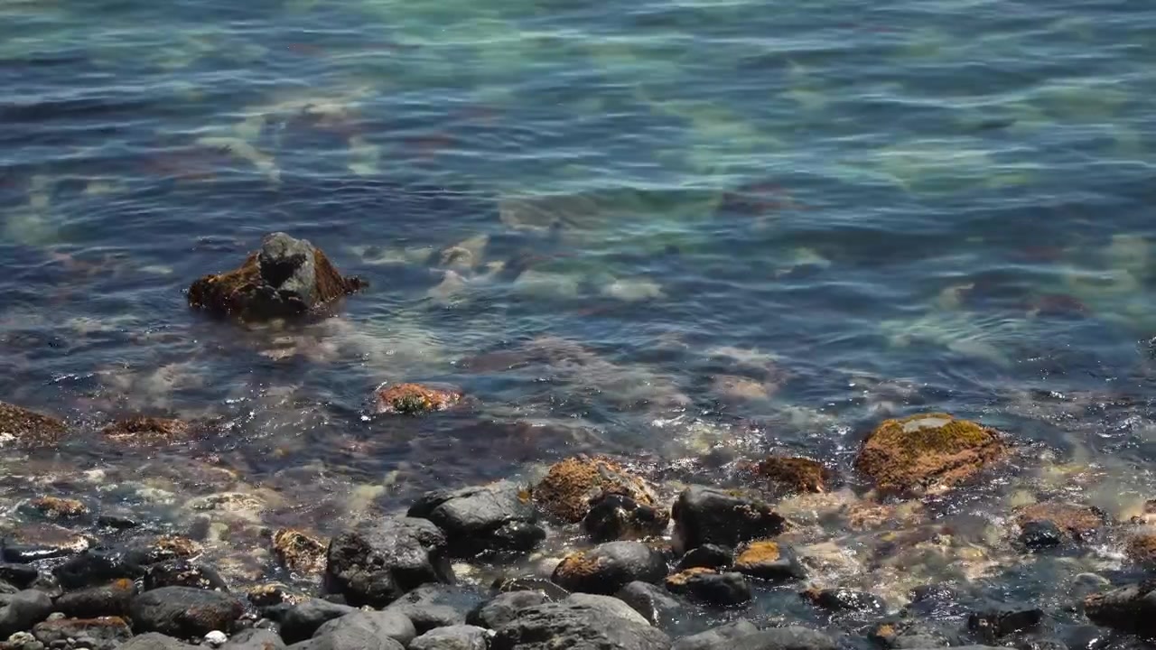 Onde delicate che si infrangono su rocce e massi con schiuma nel mare blu cristallino sulla costa rocciosa dell'Haeundae Blue Line Park a Busan, Corea del Sud