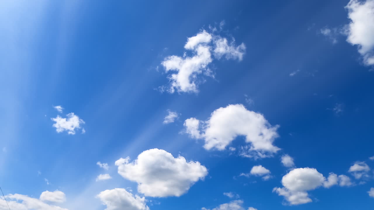 Beautiful white soft clouds changing shape in the blue sky. Sun beams cross the clouds. Low angle view. Timelapse.