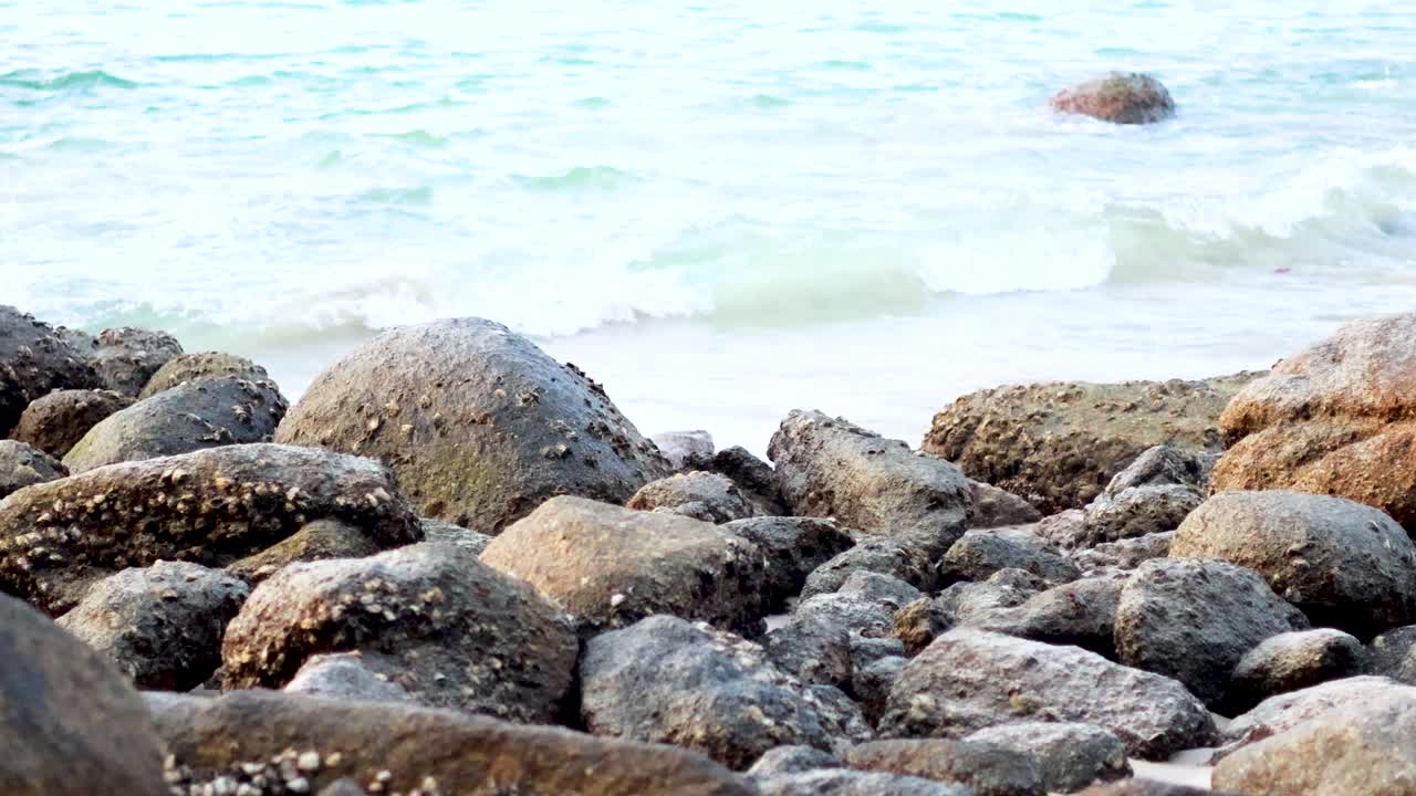 A serene view of rocks and gentle waves at Karon Beach, Phuket. Natural lighting highlights the tranquil coastal scene