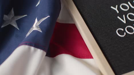 Close-Up-Of-Sign-Reading-Your-Vote-Counts-Lying-On-US-Stars-And-Stripes-Flag-For-American-Election-2024-2