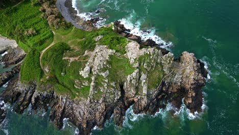 Top-down drone movement over the jagged Breton cliffs Pointe du Chateau at Trestrignel beach, Perros-Guirec, Brittany, France.
