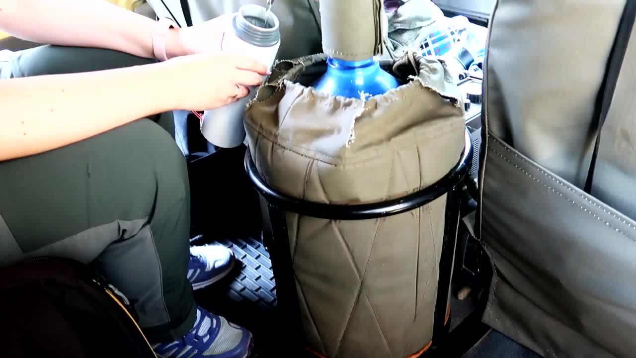 mujer sirviendo agua mineral rellenando una cantimplora dentro de un coche safari 4x4