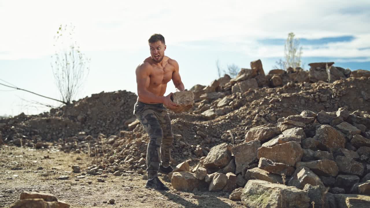 Shirtless athlete throwing stones outdoors. Young sportsman doing exercise with heavy rocks. Motion of stone flying in the air. Slow motion.