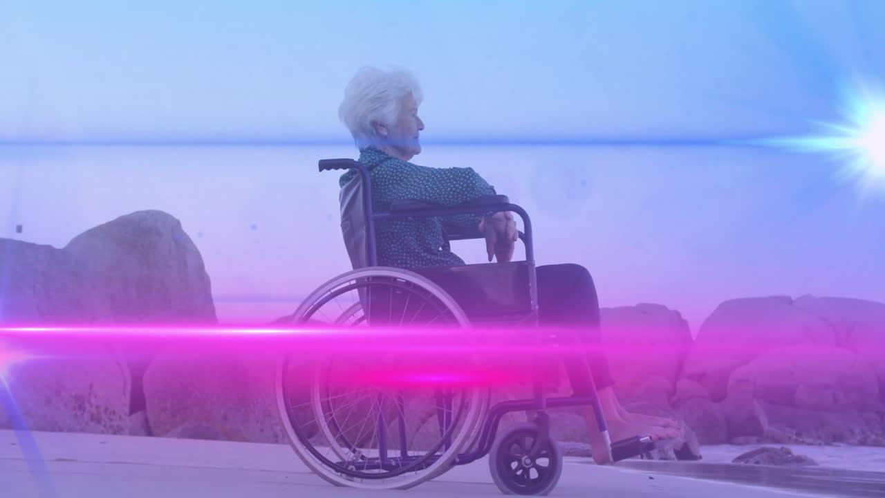 Animation of lights moving over senior caucasian woman in wheelchair on beach looking to sea
