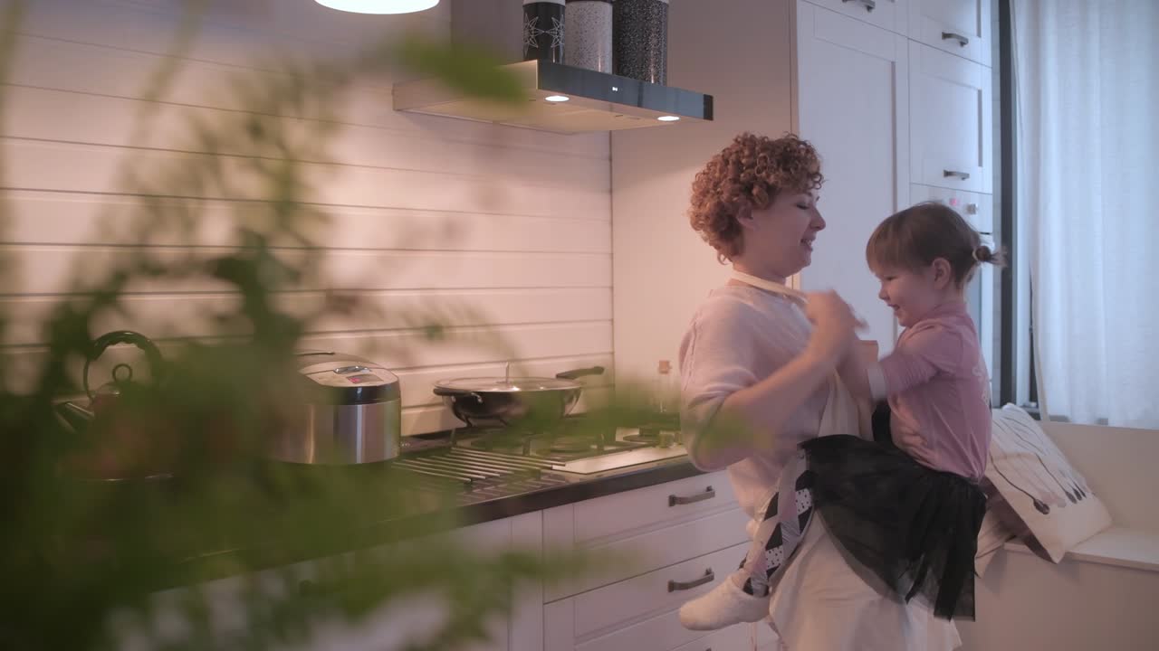 Una bambina che si diverte in cucina. Mamma e figlia si divertono insieme. La mamma fa girare la figlia. La bambina gattona intorno alla mamma. Mamma e figlia si divertono in cucina
