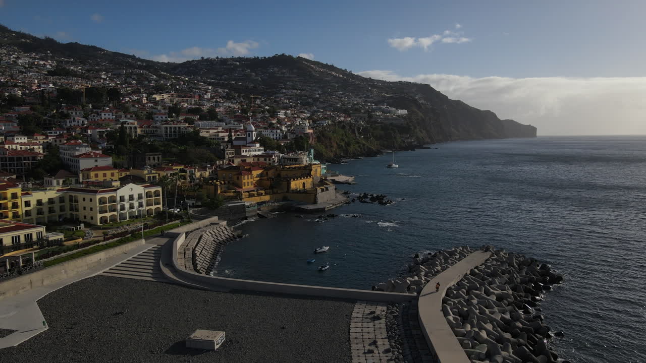 Vista aérea da doca do porto do Funchal, aproximando-se do forte da Madeira, onde se podem ver as muitas casas e edifícios da costa.