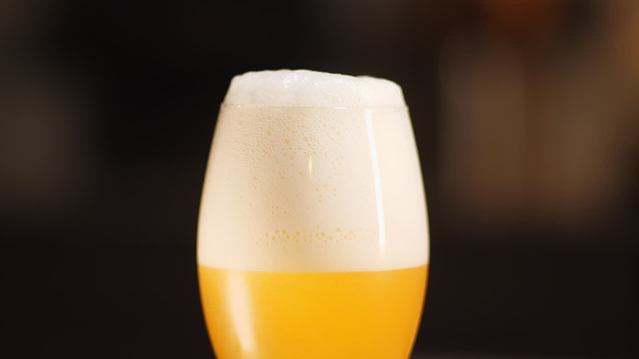 Medium shot of craft Beer being poured in to a pint glass with a lot of frothy head, dark background