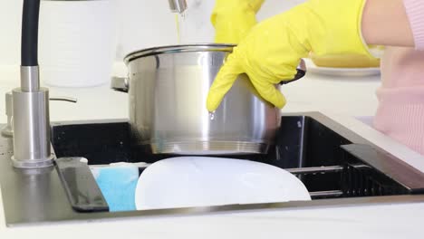 person in yellow gloves washing a pot in the kitchen sink