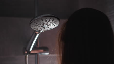 woman waits while water starts to run in shower cabin closeup. lady stands near shower head with falling liquid drops in home bathroom. body care