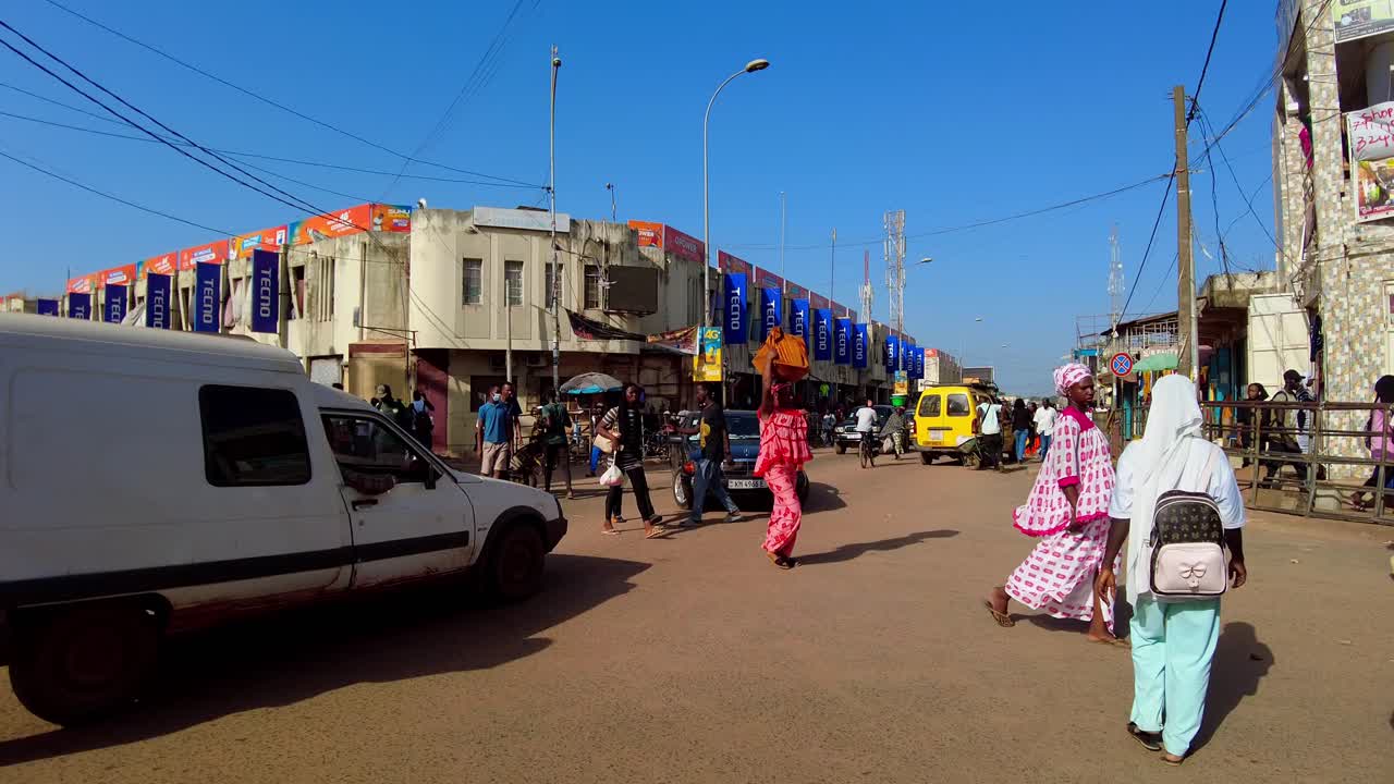 POV shot of walking on busy Serekunda Market street intersection in Gambia on a sunny day.