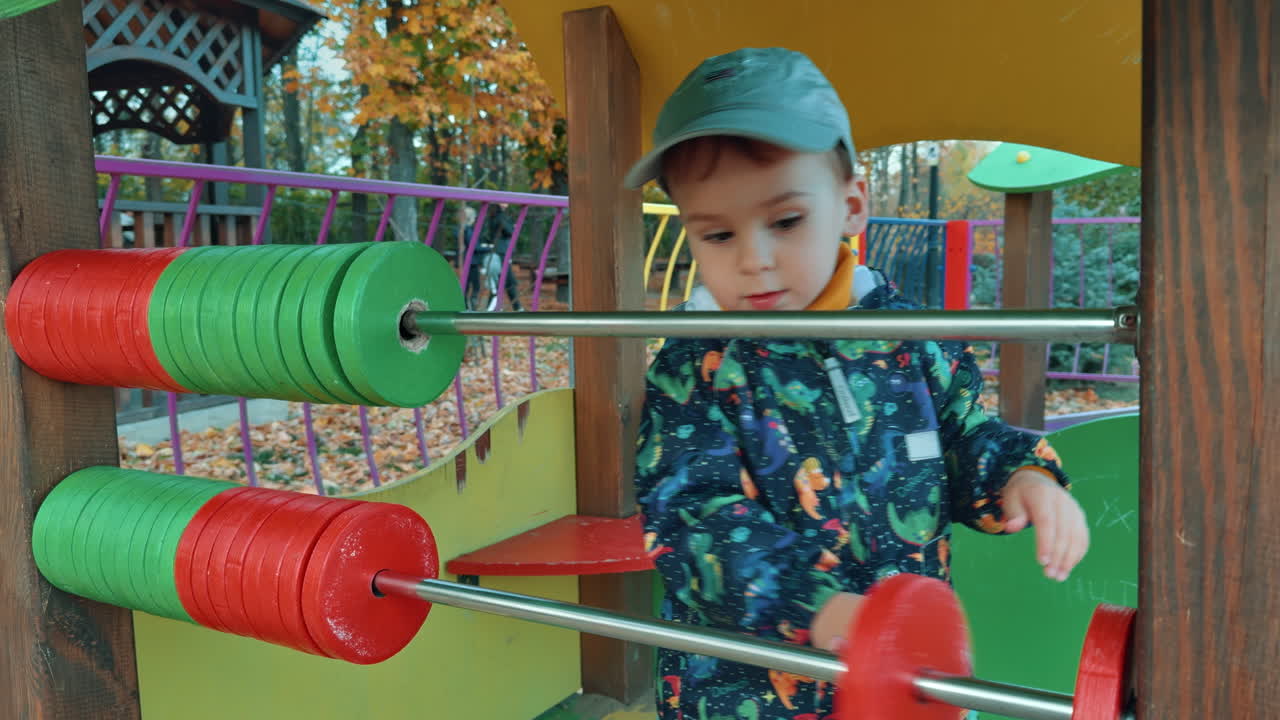 Lovely Caucasian toddler playing with big abacus on the playground. Male kid having good time outdoors in autumn.