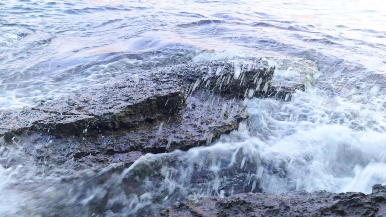 Waves crashing into rocks near Budva old town on the coastline of Montenegro on the Adriatic coastline on a sunny sunset afternoon. Slow-motion footage of waves crashing in 4k