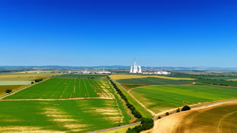 summer fields & industry. lush green fields stretch across the rural landscape showcasing a blend of agriculture and nearby industrial facilities