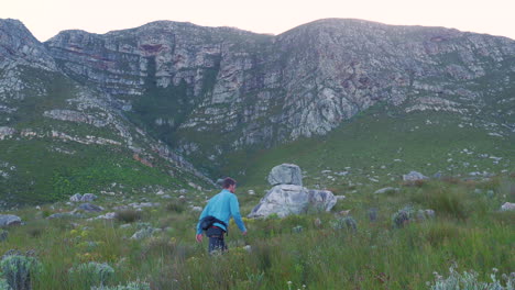 man hiking up trail next to imposing sandstone mountains, hermanus, south africa