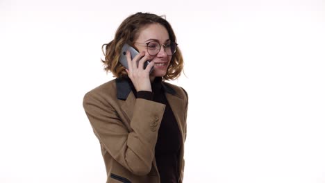 cheerful woman talking mobile phone, excited about talk on white background at studio. woman in glasses and brown jacket