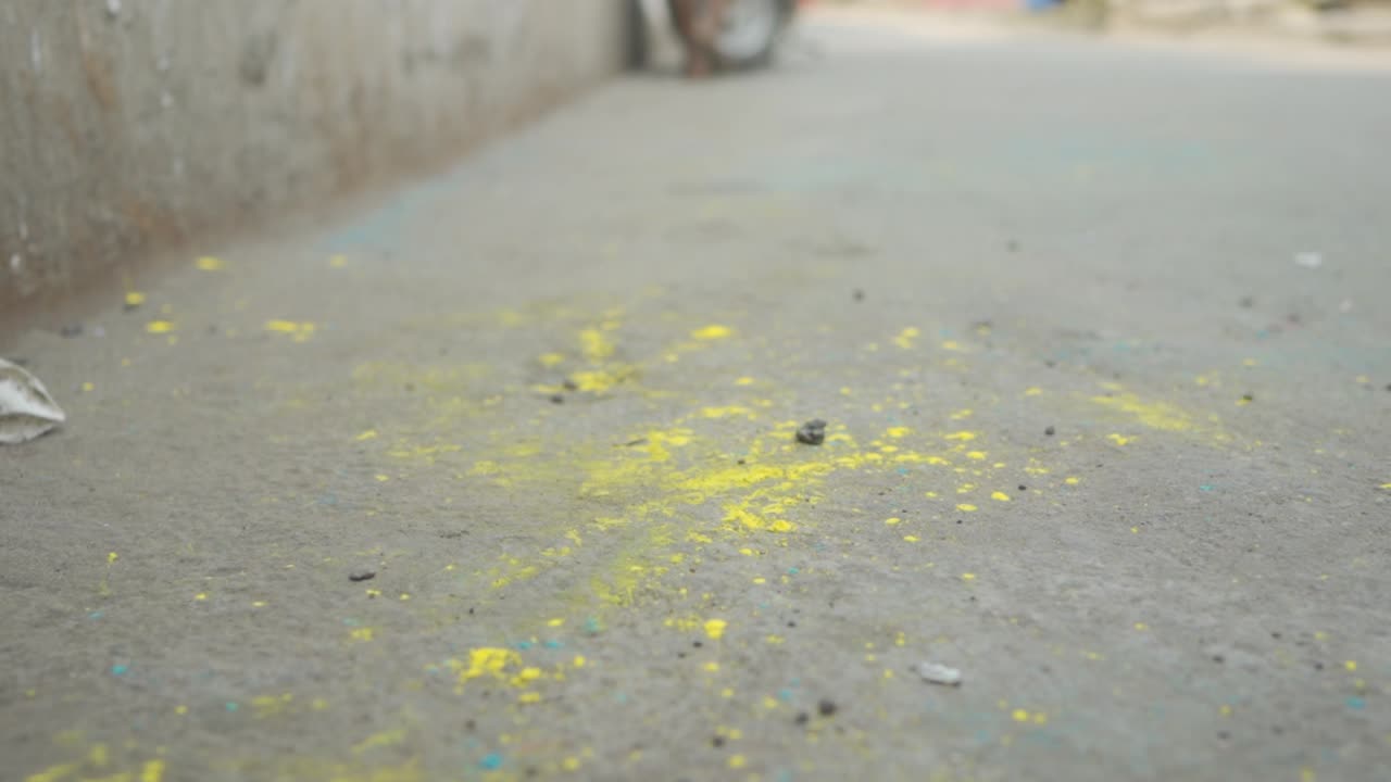 Close up of dirty feet of poor dark skin Indian girl walking away, yellow powder on feet and ground, holi festival