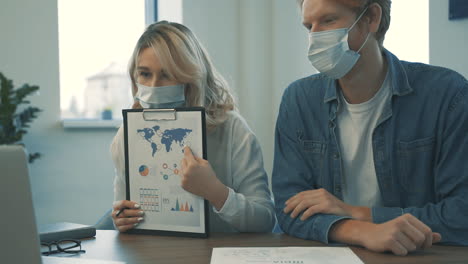 young male and female with face mask having a business video call and showing documents with charts and graphs