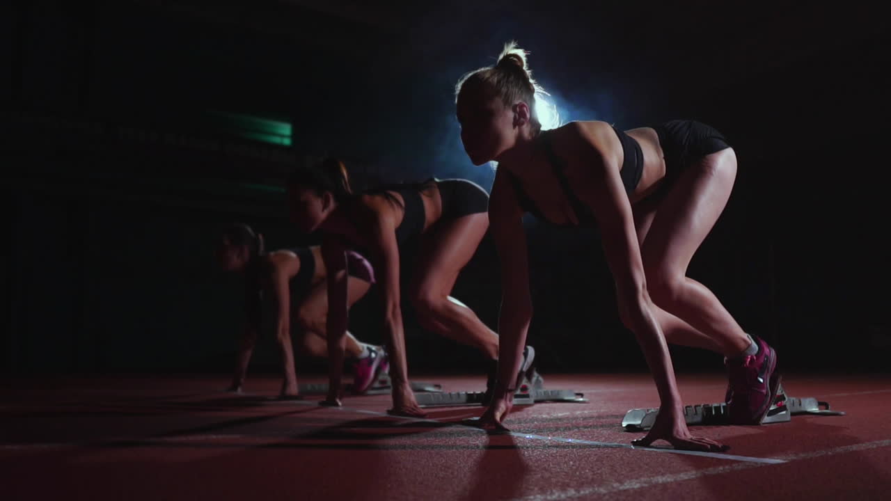 검은 옷을 입은 세 명의 소녀들이 경주를 시작하기 위해 출발 지점에서 빛의 빛에 경주를 시작하고 결승선을 향해 달리고 있습니다.