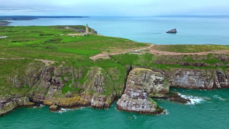 Drone pans from sea to shore revealing Cap Fréhel’s lighthouse, cliffs, hiking trails, and rugged coastline. Brittany, France