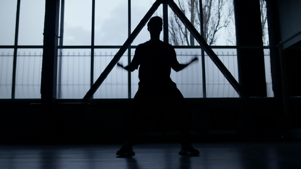 어두운 실내에서 연습하는 댄서의 실루 ⁇ . 실내에서 춤을 추는 알려지지 않은 남자.