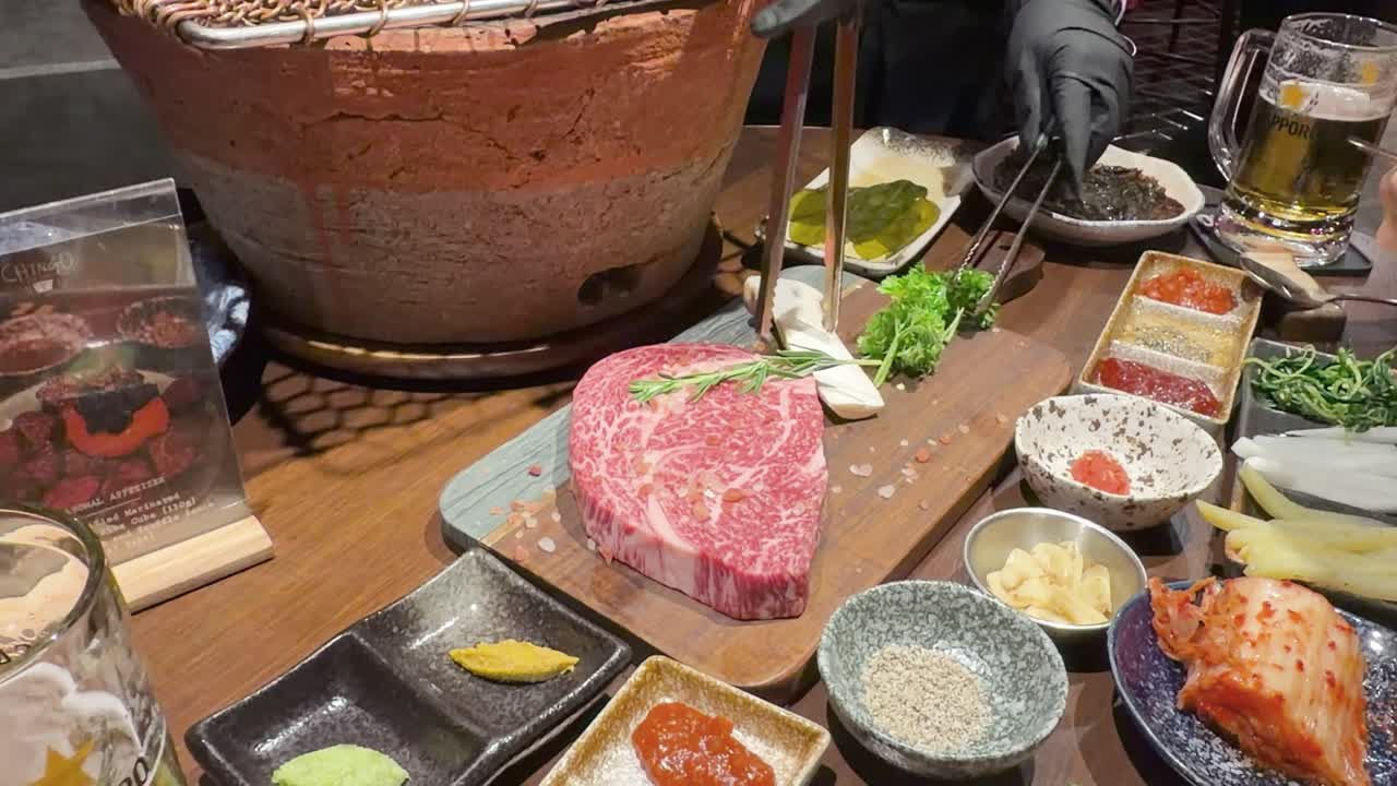 Gloved chef arranges wagyu steak and vegetables beside tabletop grill in warmly lit restaurant