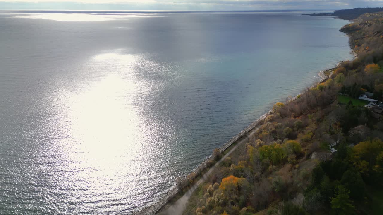 Aerial pullback over sunlight beam reflecting on ocean waves, tranquility and natural beauty enjoyed from homes on cliffs