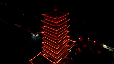 Backward-drone-on-red-illuminated-pagoda-at-night-in-Zhangjiajie-National-Forest-Park,-China