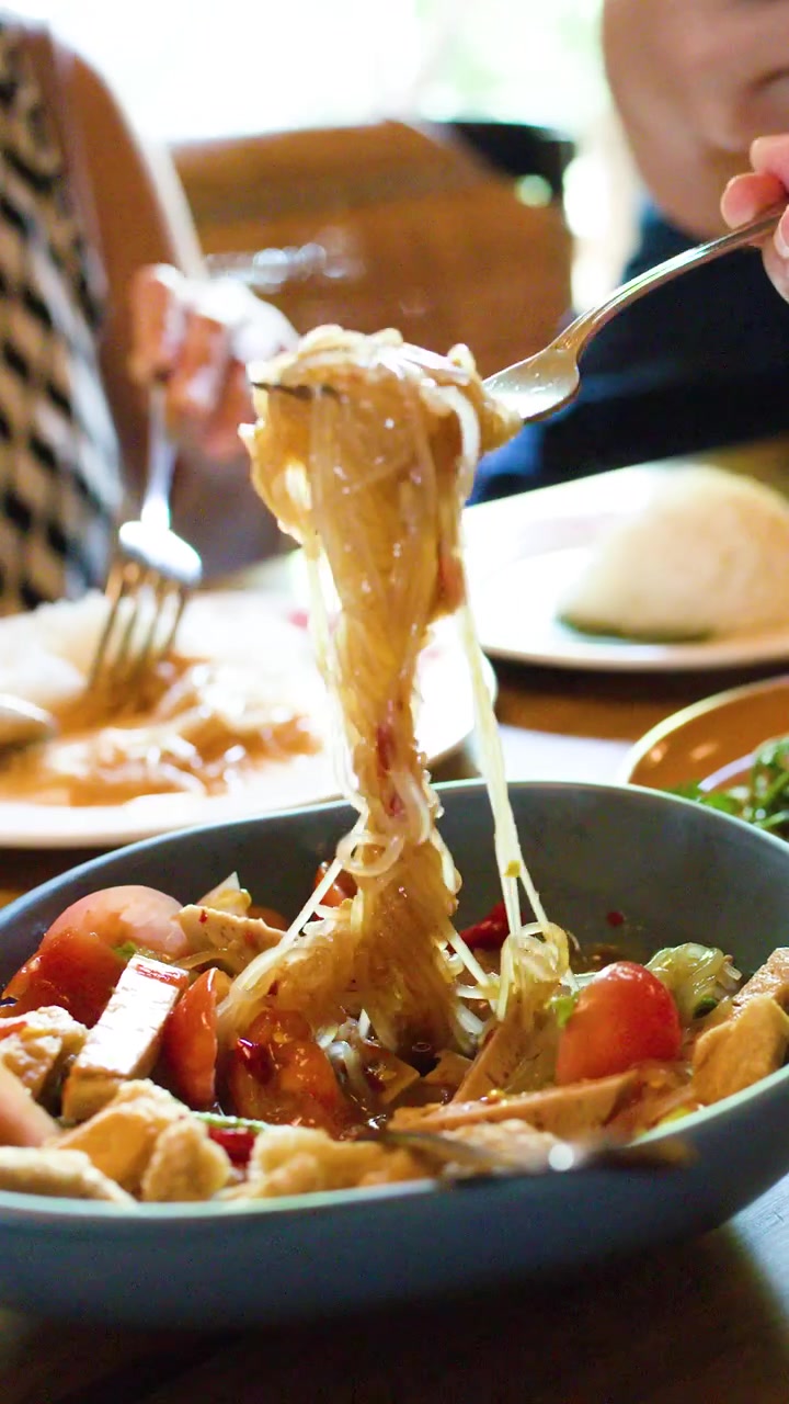 I commensali avvolgono insalata piccante di vermicelli di riso con le forchette in un ambiente luminoso e informale di un ristorante di Bangkok.