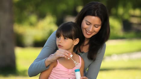 Daughter-blowing-bubbles-with-her-mother-sitting-on-the-grass