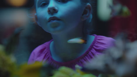 happy girl in aquarium looking at tropical fish curious child watching colorful sea life swimming in tank learning about marine animals in underwater ecosystem cute kid at oceanarium