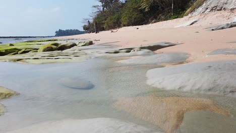 Felsenbecken-In-Den-Vulkanischen-Überresten-Der-Abgelegenen-Andamaneninsel-Strand-In-Der-Mittagssonne-Mit-Uralten-Wäldern,-Die-Das-Ufer-Säumen,-Und-Einem-Blauen-Himmel-Dahinter