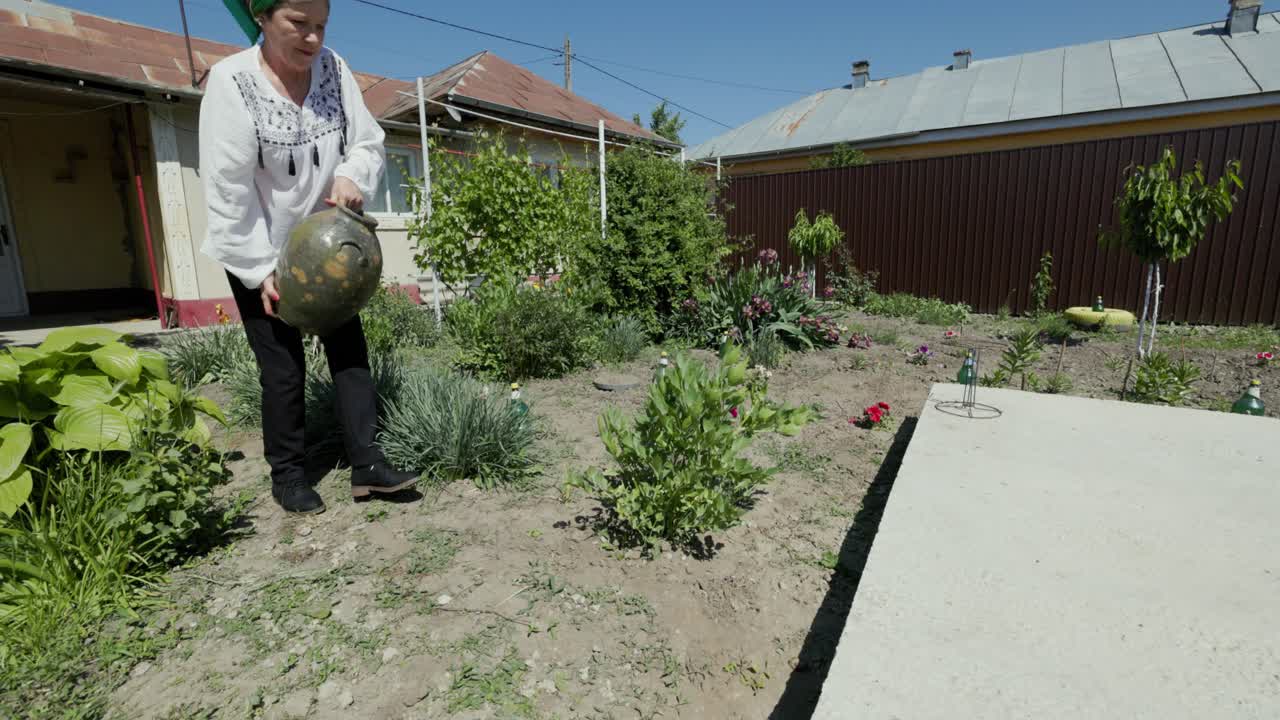 mujer rumana regando una planta en el jardín con una jarra de cerámica tradicional