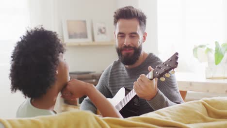 Video-De-La-Vista-Trasera-De-Una-Feliz-Pareja-Diversa-En-Casa,-Un-Hombre-Tocando-La-Guitarra,-Cantándole-A-Una-Mujer,-Copiando-Espacio