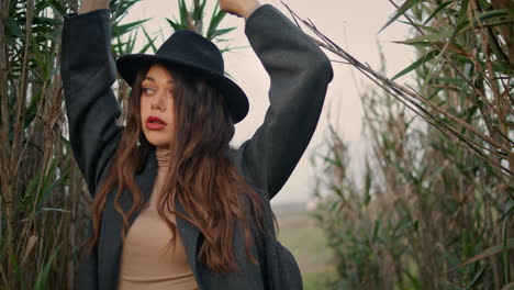 Girl-standing-high-grass-in-black-hat-close-up.-Woman-raising-hands-posing.