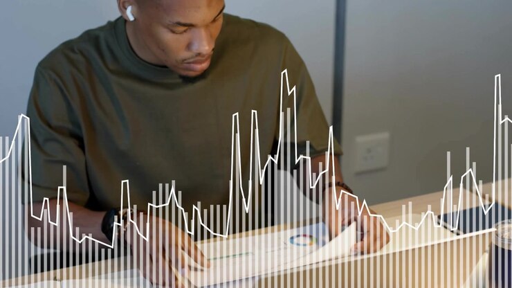 Man at desk reaching for pad sorting lifting finance chart reviewing page with waveform overlay