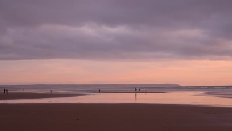 Gente-Disfrutando-De-Una-Tranquila-Y-Relajante-Puesta-De-Sol-En-La-Playa-Con-Reflejos-Coloridos