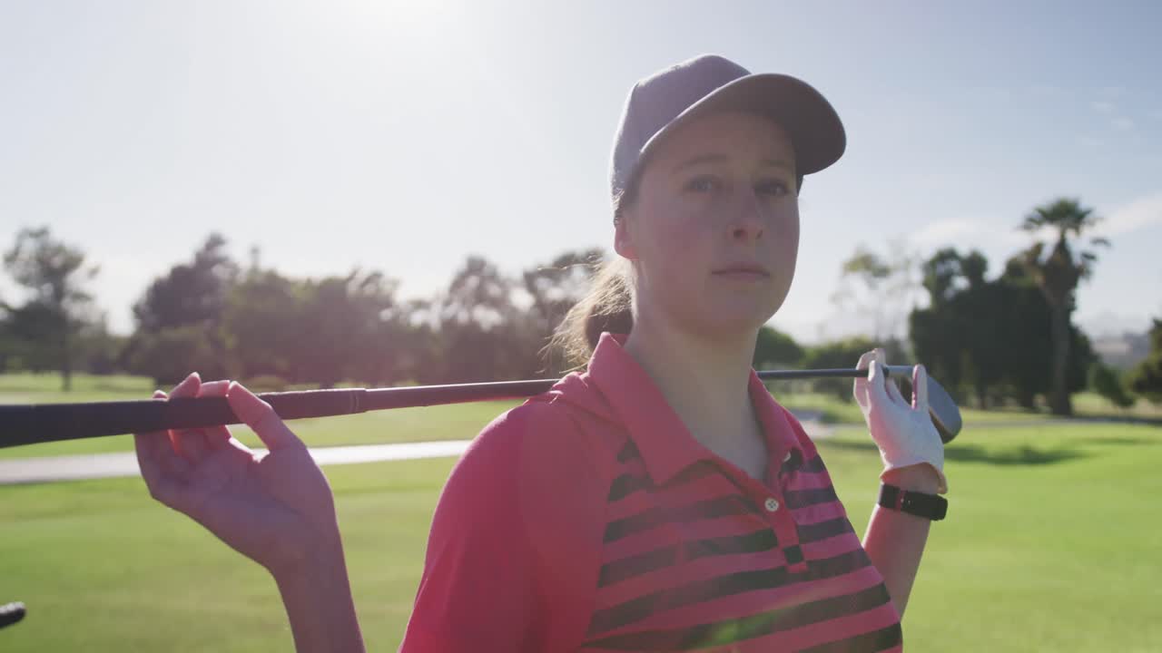 여자 백인 골프 선수 의 초상화 가 골프 클럽 을 가지고 뒤 에 서서 미소 짓고 있다
